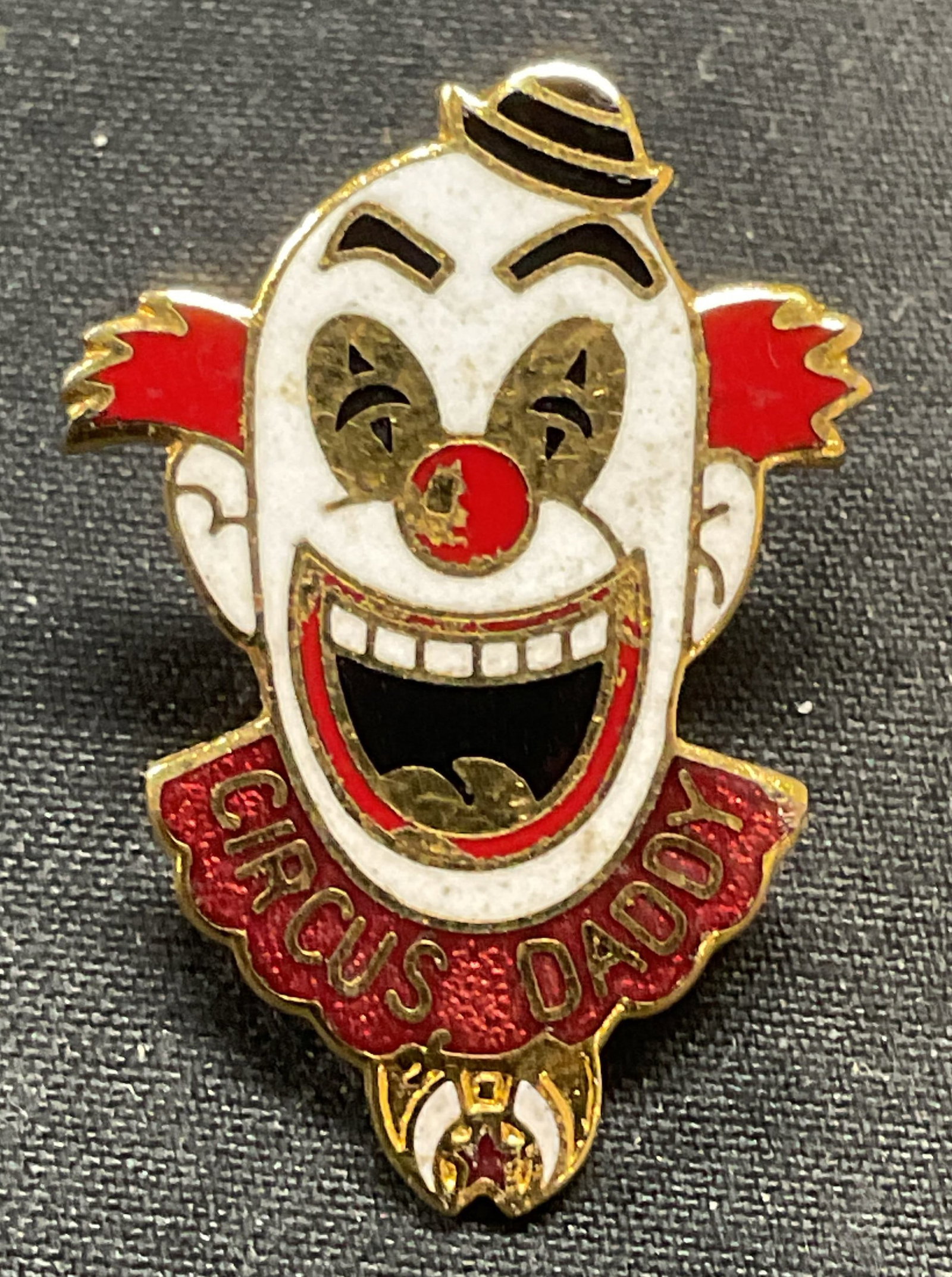 Gold Tone Enameled Circus Clown Head Pin: Gold tone clown head motif pin. Enamel decoration in white, red, and black. Reads Circus Daddy. Measures approx. 1 x .75 inches. Some surface wear including scratching observed. Estate jewelry, costum