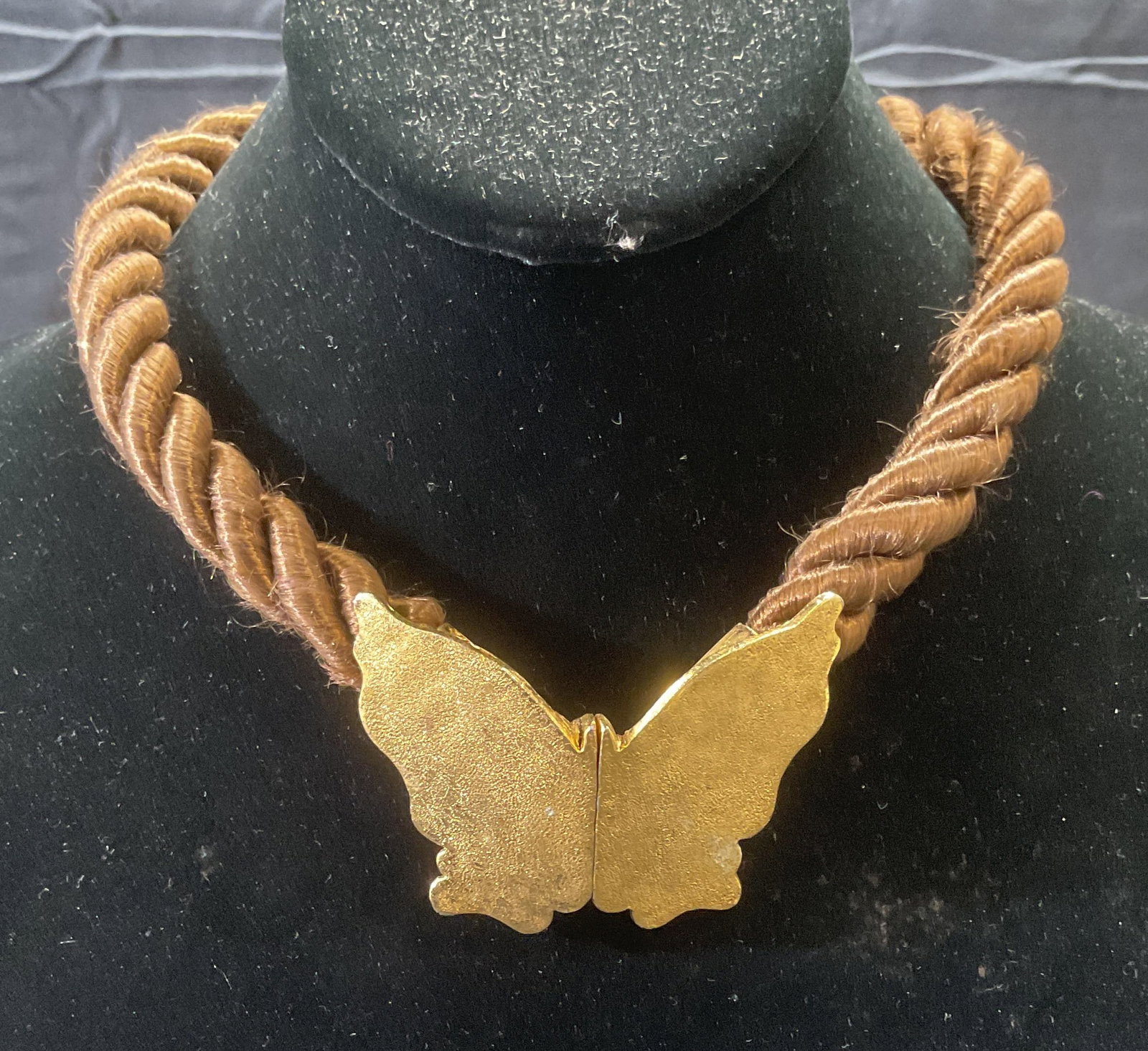 Gold Tone Butterfly Pendant Choker Necklace: Gold tone butterfly clasp pendant necklace with twisted brown cord. Drop length approx. 7 inches. Butterfly measures approx. 1.75 x 2.5 inches. Some surface wear including scratching observed. Jewelry