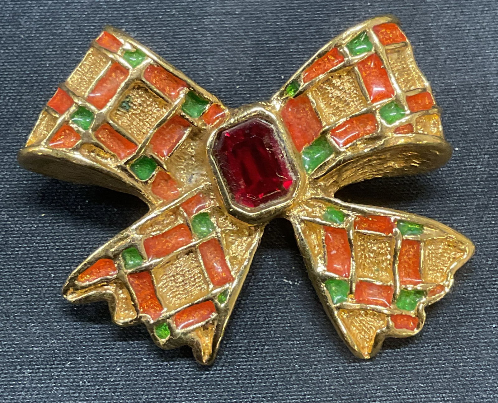 Yves Saint Laurent Gold Tn Crystal Bow Brooch: Yves Saint Laurent gold tone bow motif brooch with enamel and red crystal decoration. Signed to underside. Made in France. Hinge pin to underside. Measures approx. 1.25 x 1.5 inches. Some surface wear