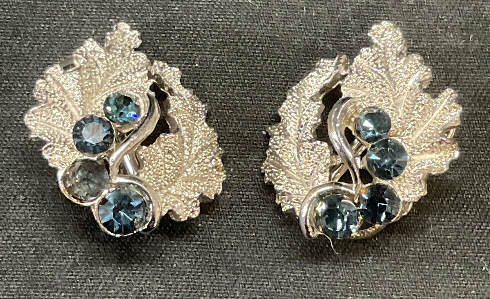 Trifari Silver Tn Blue Crystal Botanical Earrings: Trifari silver tone botanical leaf motif clip on earrings with blue crystal decoration. Signed on backing. Measure approx. .75 inches long. Some surface wear including scratching observed. Estate jewe