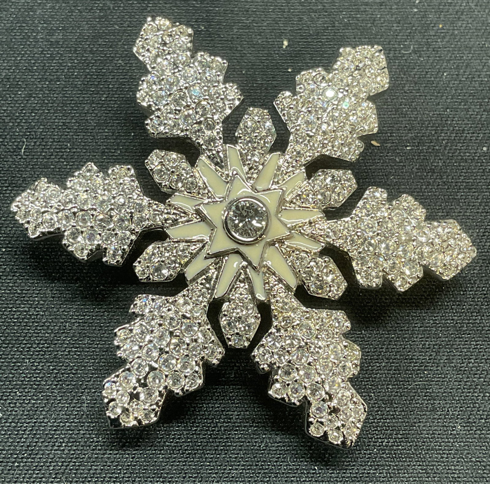 Swarovski Gold Plated Crystal Snowflake Brooch: Swarovski gold plated snowflake motif brooch. Pave colorless crystal and white enamel decoration. Signed to underside. Hinge pin to underside. Measures approx. 1.75 inches wide. Some surface wear incl