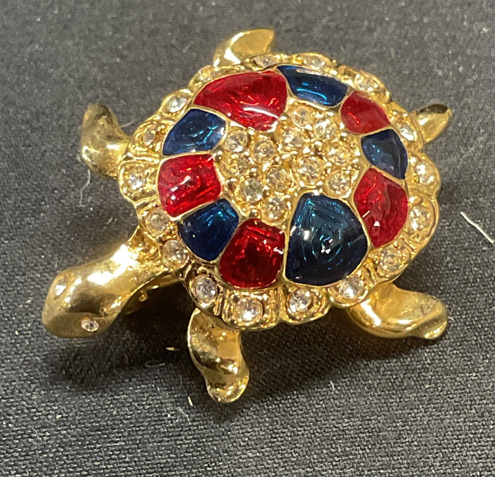 Gold Tone Enameled Crystal Turtle Brooch: Gold tone turtle motif brooch with blue and red enamel and colorless crystal decoration. Hinge pin to underside. Measures approx. 1.25 x 1 inches. Some surface wear including scratching observed. Jewe