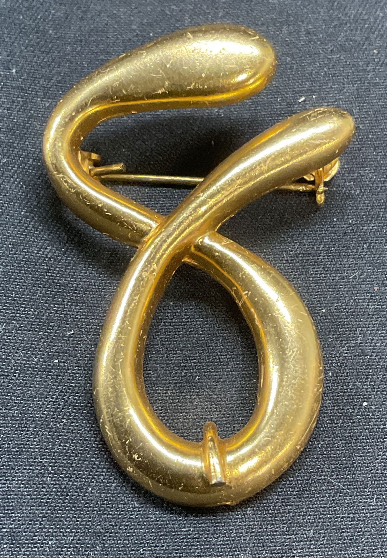 Gold Tone Squiggle Brooch: Gold tone squiggle motif brooch. Hinge pin to underside. Measures approx. 1.75 x 1.25 inches. Some surface wear including scratching and chipping observed. Jewelry, estate jewelry, costume jewelry, co