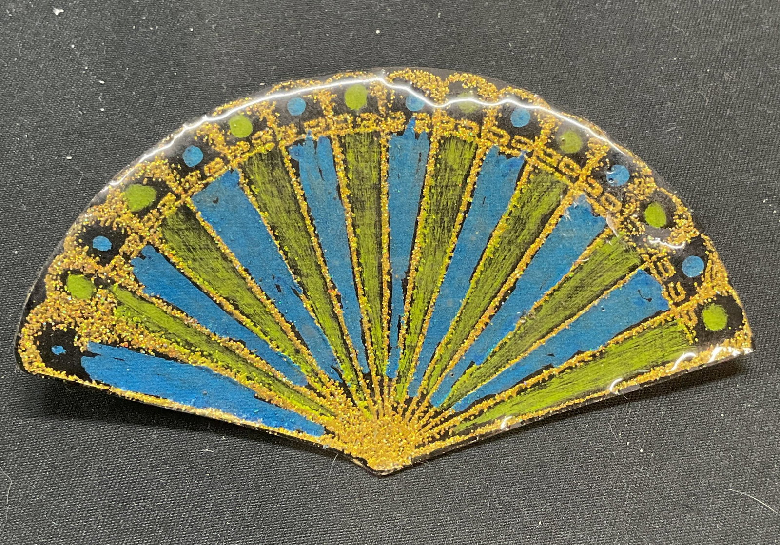 Hand Painted Lacquered Fan Brooch: Hand painted lacquered fan motif brooch in green, blue, and gold. Lacquer over paper. Hinge pin to underside. Marked 2002. Measures approx. 3.75 x 2 inches. Some surface wear including scratching and 