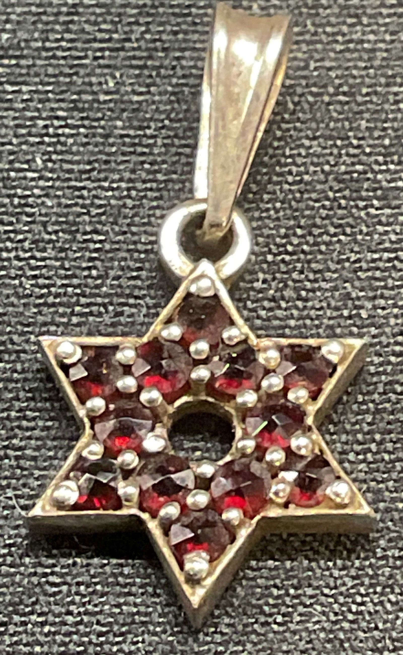 Sterling Silver & Garnet Star of David Pendant: Sterling silver and red garnet gemstone decorated Star of David motif pendant, marked 925, additional mark reads G. Measures approx. 3/8 inches wide. Total weight .9 grams. Some surface wear including
