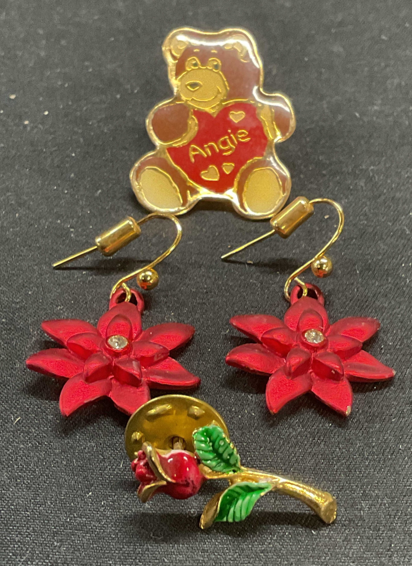 Lot 3 Poinsettia Earrings, Teddy Pin, Rose Pin: Lot of 3 jewelry pieces. Red poinsettia motif and crystal dangle earrings. Hook backing. Measure approx. 1 inch wide. Swib enameled teddy bear motif pin, reads Angie. Enameled rose motif pin. Larger p