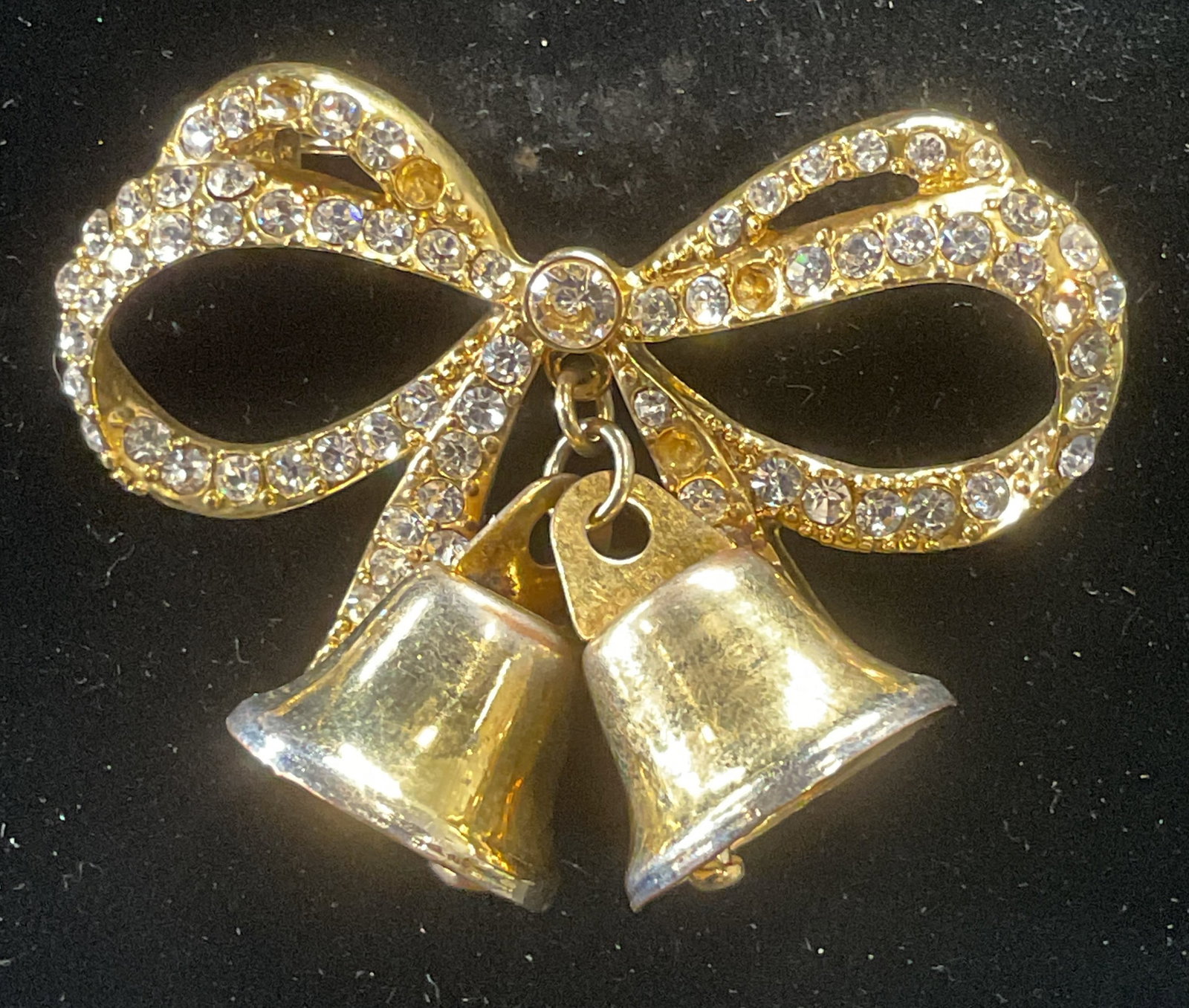Vintage Monet Gold Tn Crystal Bell Bow Brooch: Vintage Monet gold tone bow motif brooch with bell decoration and colorless crystal accents. Signed to underside. Hinge pin to underside. Measures approx. 1.5 x 2.25 inches. Some surface wear includin