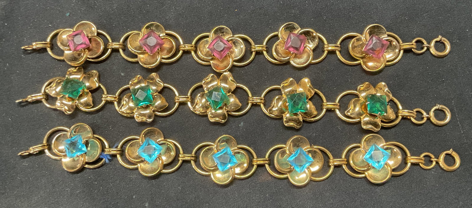 Lot 3 Gold Filled Crystal Flower Bracelets: Lot of 3 gold filled bracelets with flower motif panels and purple, blue, and green crystal decoration. All measure approx. 7 inches long. Some surface wear to all pieces including scratching observed