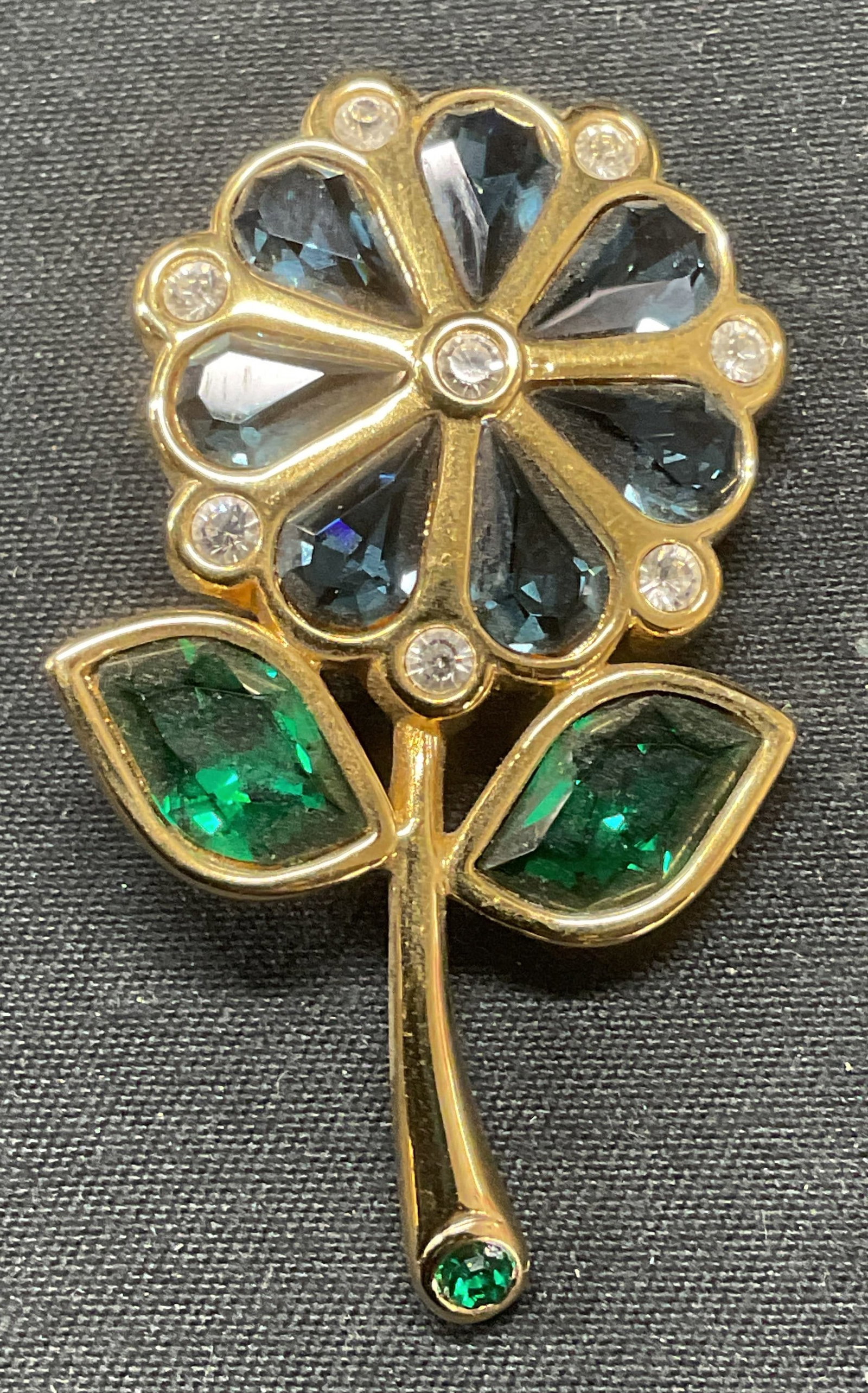 Swarovski Crystal Flower Gold Pl Brooch: Swarovski flower motif gold plated crystal brooch. Blue, green, and colorless crystal. Signed to underside. Hinge pin to underside. Measures approx. 1.75 x 1 inches. Some surface wear including scratc