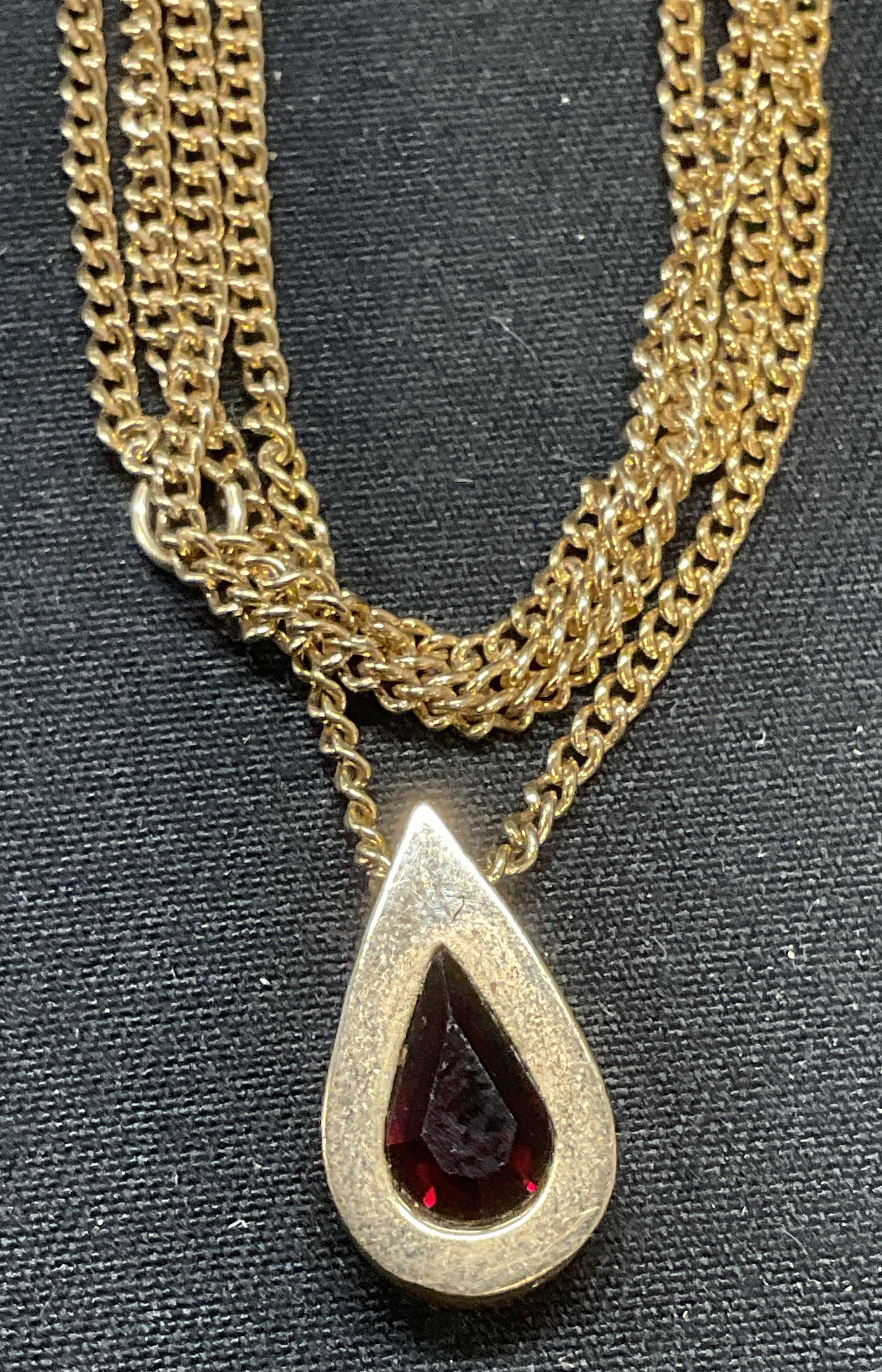 Vintage Avon Gold Tone Crystal Pendant Necklace: Vintage Avon gold tone necklace with teardrop shaped pendant and red crystal. Signed on hang tag. Drop length approx. 9.25 inches. Pendant measures approx. 5/8 inches long. Some surface wear including