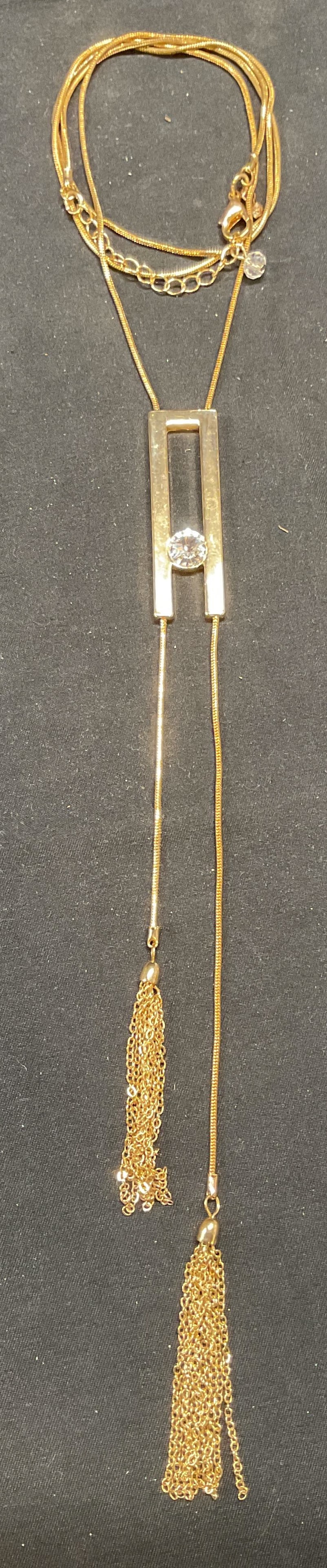 Gold Tone Crystal Pendant Necklace: Gold tone snake chain necklace with crystal, chain, and tassel pendant. Necklace drop length approx. 15.25 inches, total pendant drop length approx. 8.5 inches. Some surface wear including scratching 