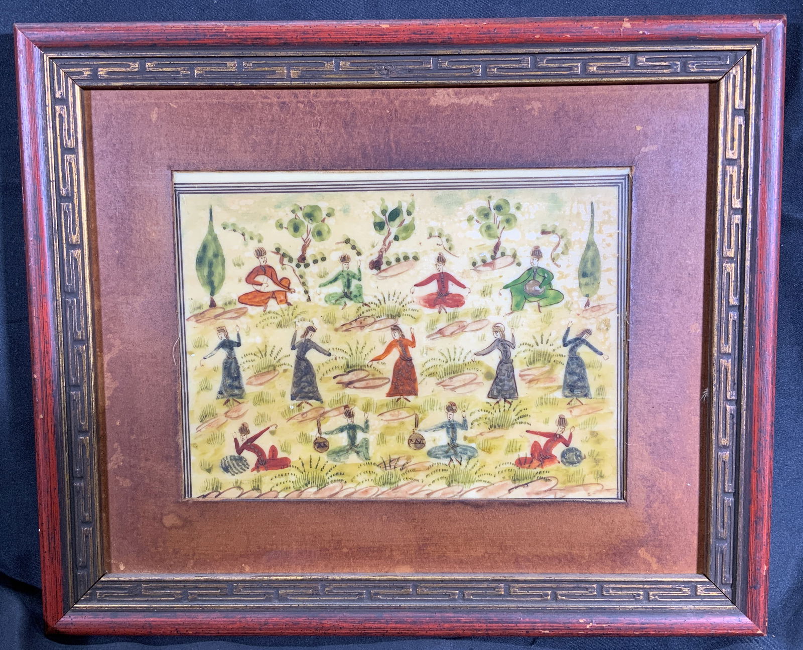 Framed Hand Painted Dancing Gathering: Hand painted on composite tile. Subject depicts a gathering of people dancing and playing instruments. Framed in gilt wooden frame with patterned motif. Frame measures approx. 12 W x 10 H in. Window m
