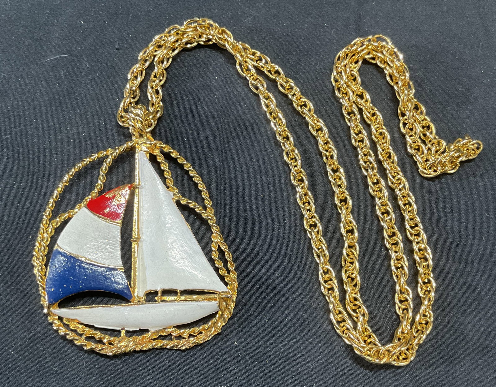 Gold Tone Sailboat Pendant Necklace: Gold tone chain necklace with sailboat motif pendant. Painted decoration in white, red, and blue. Drop length approx. 15 inches. Pendant measures approx. 2.5 inches long. Piece has weight. Some surfac