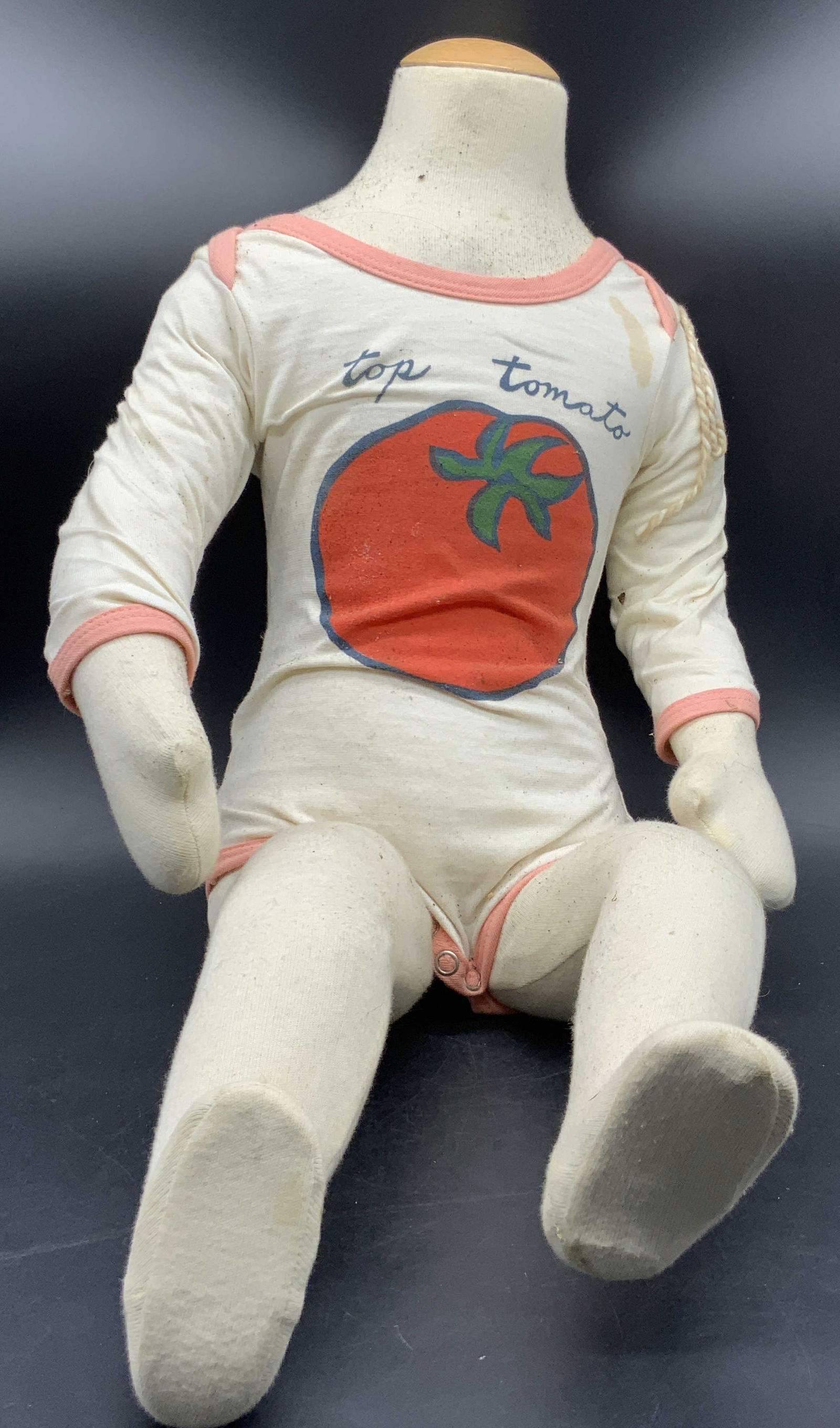 Fabric Child Size Mannequin W/ Articulated Limbs: A fabric child size mannequin with articulated limbs. Zipper to reverse. Measures approx. 25L x 12.5W in. Mannequin wears a removable onesie with a tomato motif. Discoloration, residue, tearing, and l