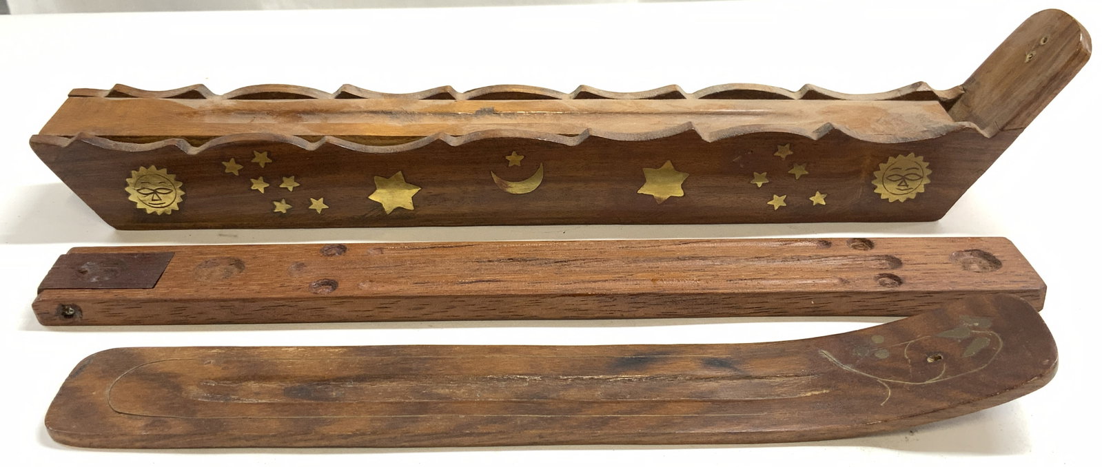 Lot 3 Wood & Brass Inlay Incense Burners: Lot includes 1 incense burner with sun, star and moon brass inlay, 1 flat wooden incense burner, and 1 incense burner with one curved end. Largest piece is lot measures approximately 14 inches long 2.