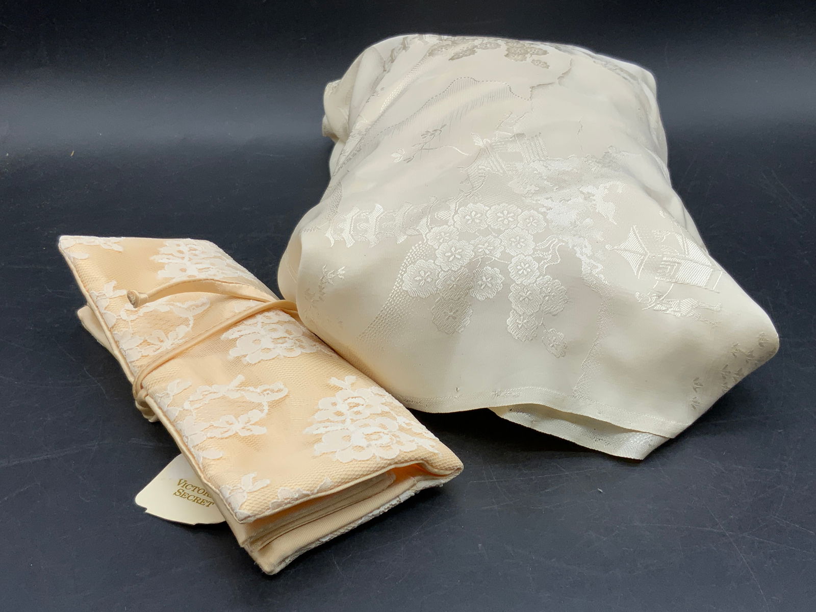 Lot 2 Victorias Secret Pouch & Chinoiserie Textile: A chinoiserie textile and a Victorias Secret pouch. Both pieces are crafted from soft hand fabric. Original tag attached to the pouch. Textile Measures approx. 27W x 171L in. Tearing to the textile pr