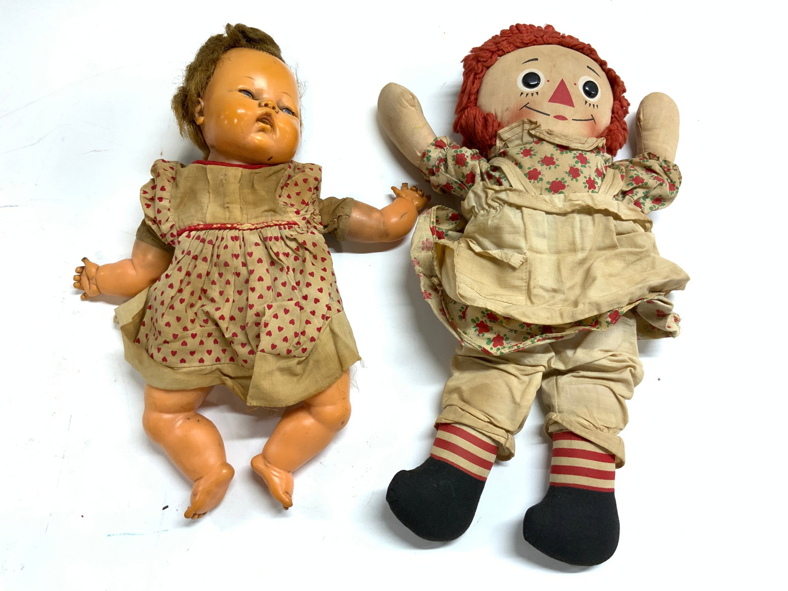 Lot 2 Vintage Baby & Raggedy Ann Doll: Lot includes 1 baby doll with floral pattern dress & 1 raggedy Ann doll. Each doll is vintage. Raggedy Ann doll has floral and leaf pattern detail. Raggedy Ann doll measures approximately 15 inches ta