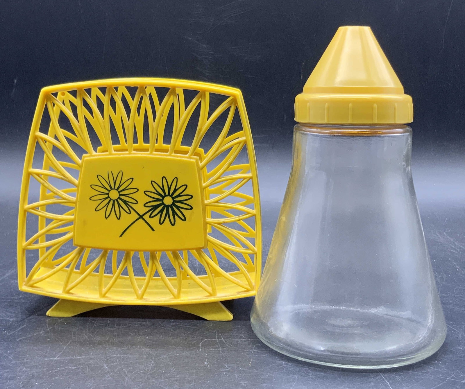 Lot 2 Vintage Yellow Kitchenware, Napkin Holder +: Two pieces of vintage kitchenware. The glass vessel with the yellow plastic lid is marked MADE IN USA, ANDROCK on the underside. Measures approx. 6.25H x 3.5W in. The napkins holder is crafted from a