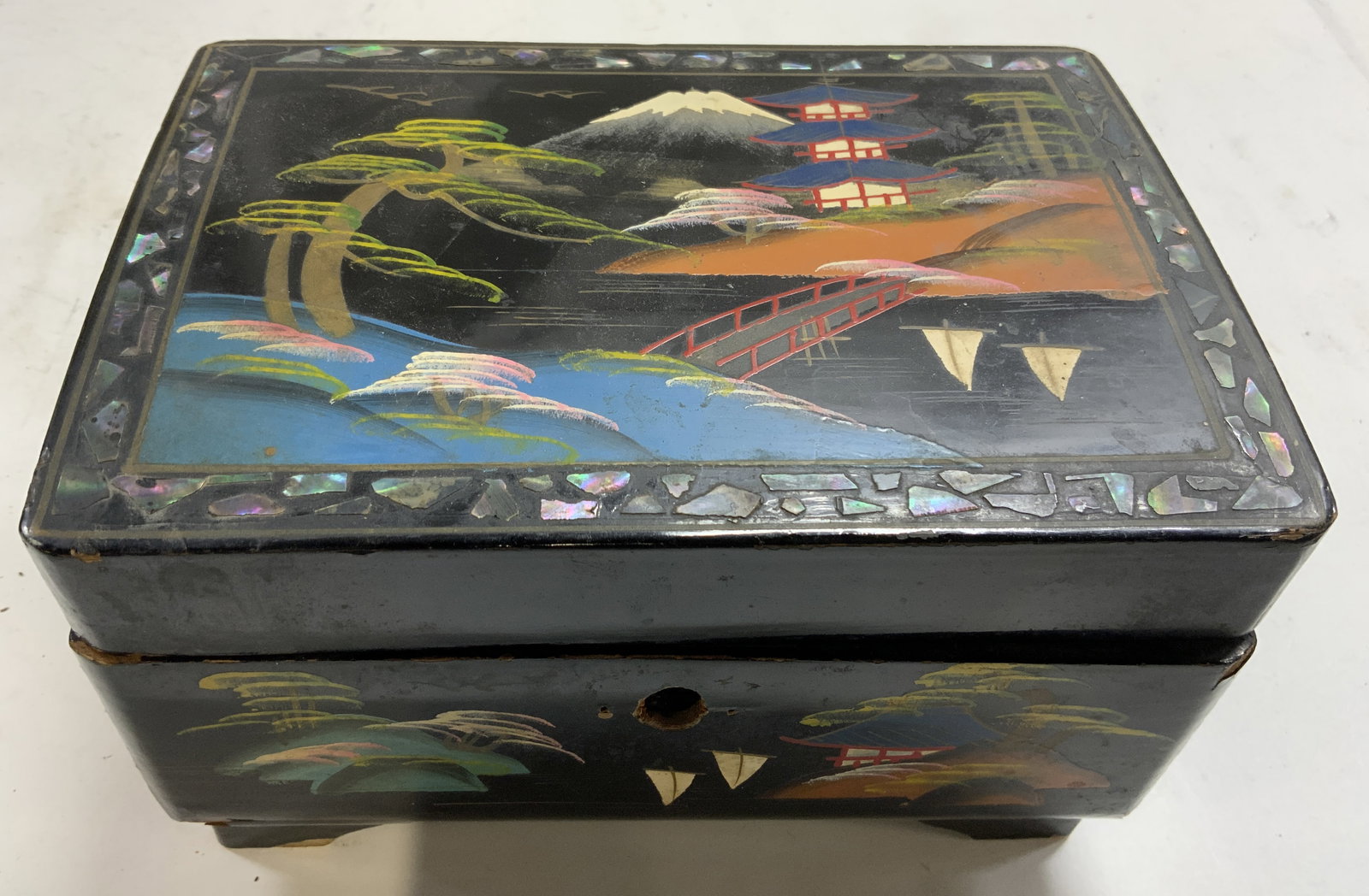 Vntg Painted Lacquered Asian Musical Jewelry Box: Musical jewelry box is black toned a lacquered. Piece has hand painted Asian architecture and landscape detail. Lid edges have mother of pearl detail. Box has hinged lid. Piece opens and has second li