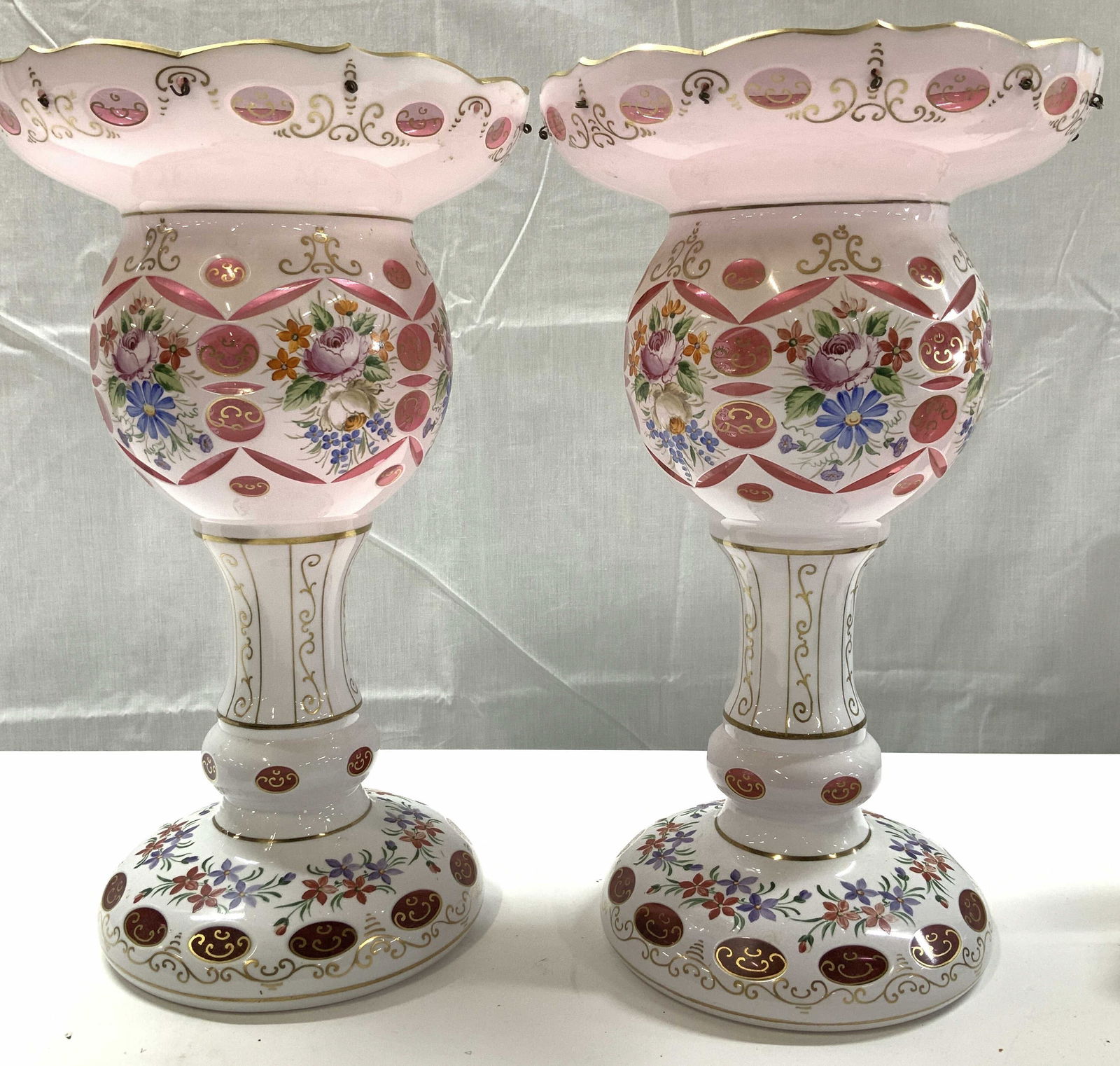 Pair Bohemian Milk Glass to Cranberry Lusters: Boheme Czechoslovakian Table / Mantle lusters in milk glass over cranberry glass, hand painted with gilt and flowers. Each measures 13 in. Ht x 7.5 in. Diameter. No crystals. Possibly 19th century. Ha