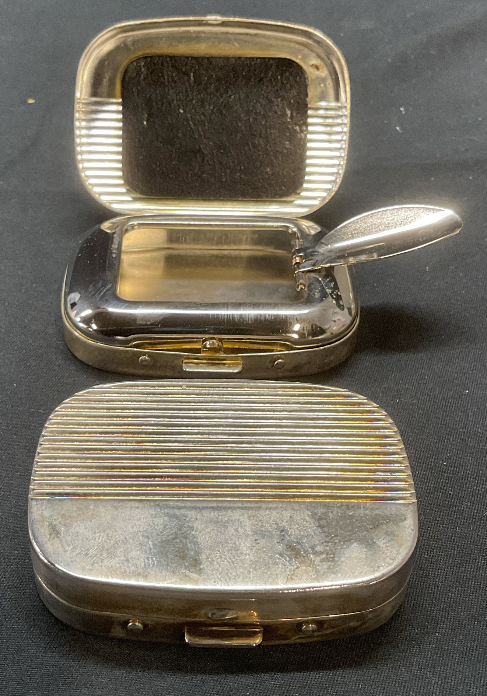 Pair Vintage Silver Plated Portable Ashtrays: Pair of vintage silver plated portable ashtrays. Ribbed detail on case. Measure approx. 2.5 x 1.75 x .75 inches each. Both pieces have some surface wear including patina and scratching observed. Ashtr