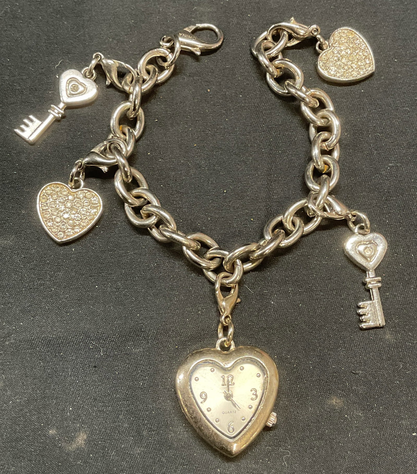 Silver Tone Heart Watch Charm Bracelet: Viler tone chain bracelet with heart motif watch and heart and key motif charms. Colorless crystal decoration. Measures approx. 7 inches long. Watch measures approx. 1 x 1 inches. Watch not tested for