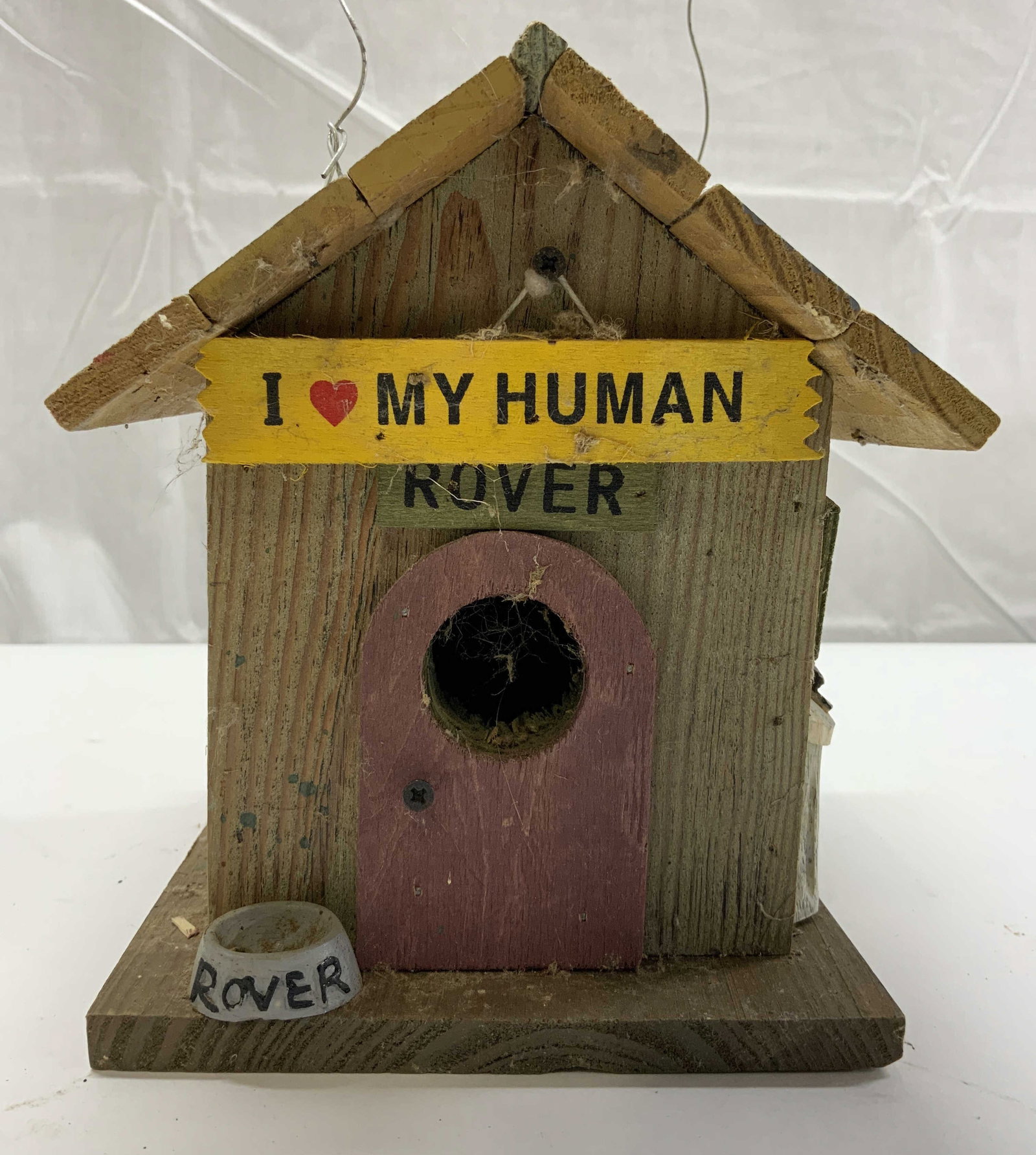 Wooden Dog House Bird House: Birdhouse is wooden. Piece appears to be vintage. Birdhouse has signs such as I heart my human Rover Cats Keep Out & Beware of Dog Birdhouse has wire for hanging. Piece measures approximately 6.5 inch