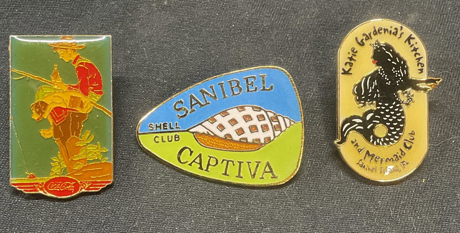 Lot 3 Vintage 1987 Coca Cola Enamel Pin +: Lot of 3 vintage enamel pins. 1987 Coca Cola pin with figural motif, Sanibel Captiva Shell Club pin with shell motif, and Katie Gardenias Kitchen and Mermaid Club Pin with mermaid motif. Coca Cola pin