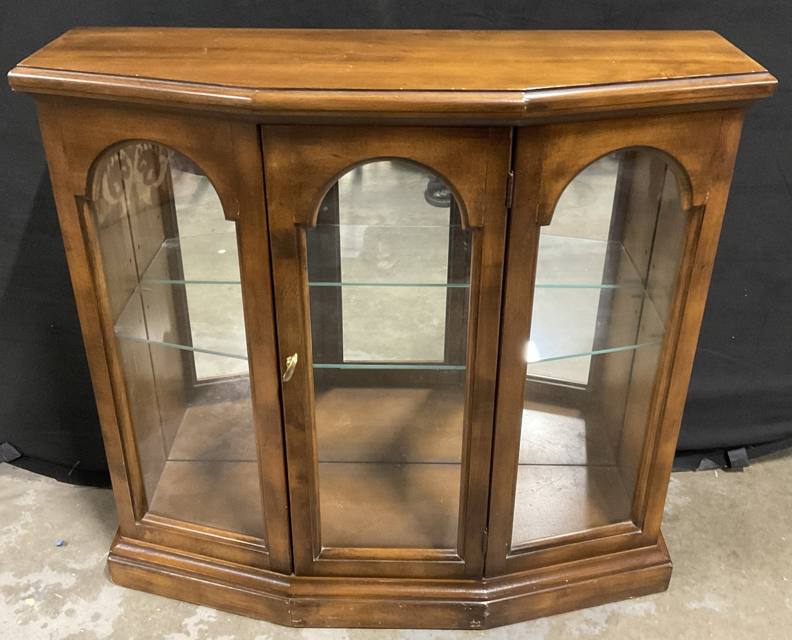 BUTLER SPECIALTY Vintage Lighted Curio Cabinet: A vintage curio cabinet crafted from wood and glass. Door to obverse features a brass handle. Mirrored backing to the cabinet interior as well as a removable glass shelf. Tags to reverse read BUTLER S