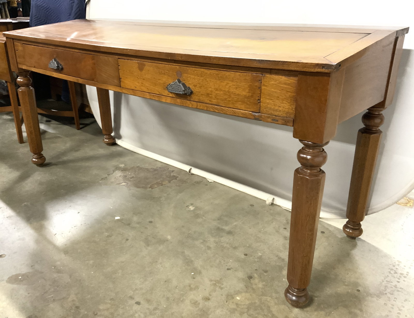 Vintage Wooden Writers Desk W Drawers: Writers desk is tan toned and wooden. Piece has 2 drawers each with bronze toned metal drawer pulls and hand dovetailing. Front of desk slopes slightly downwards to write. Desk has 4 turned wooden leg