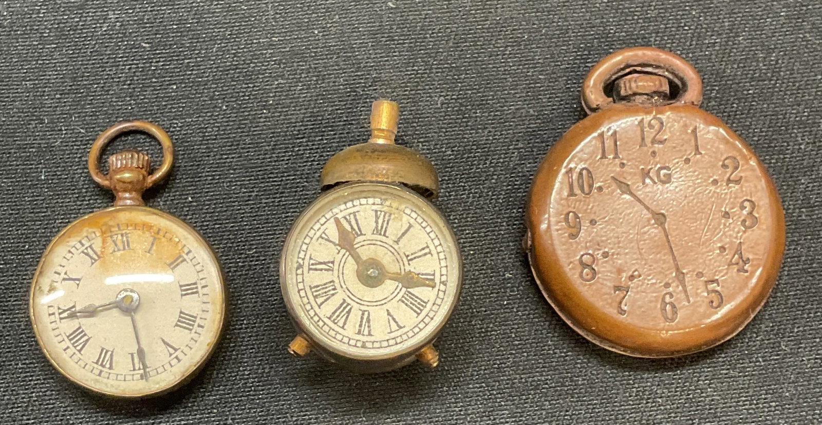 Lot 3 Vintage Watch Motif Pendants: Lot of 3 vintage watch motif pendant. 1 piece with compass to reverse. Largest measures approx. .75 inches diameter. All pieces composed of metal. All pieces have surface wear including scratching obs