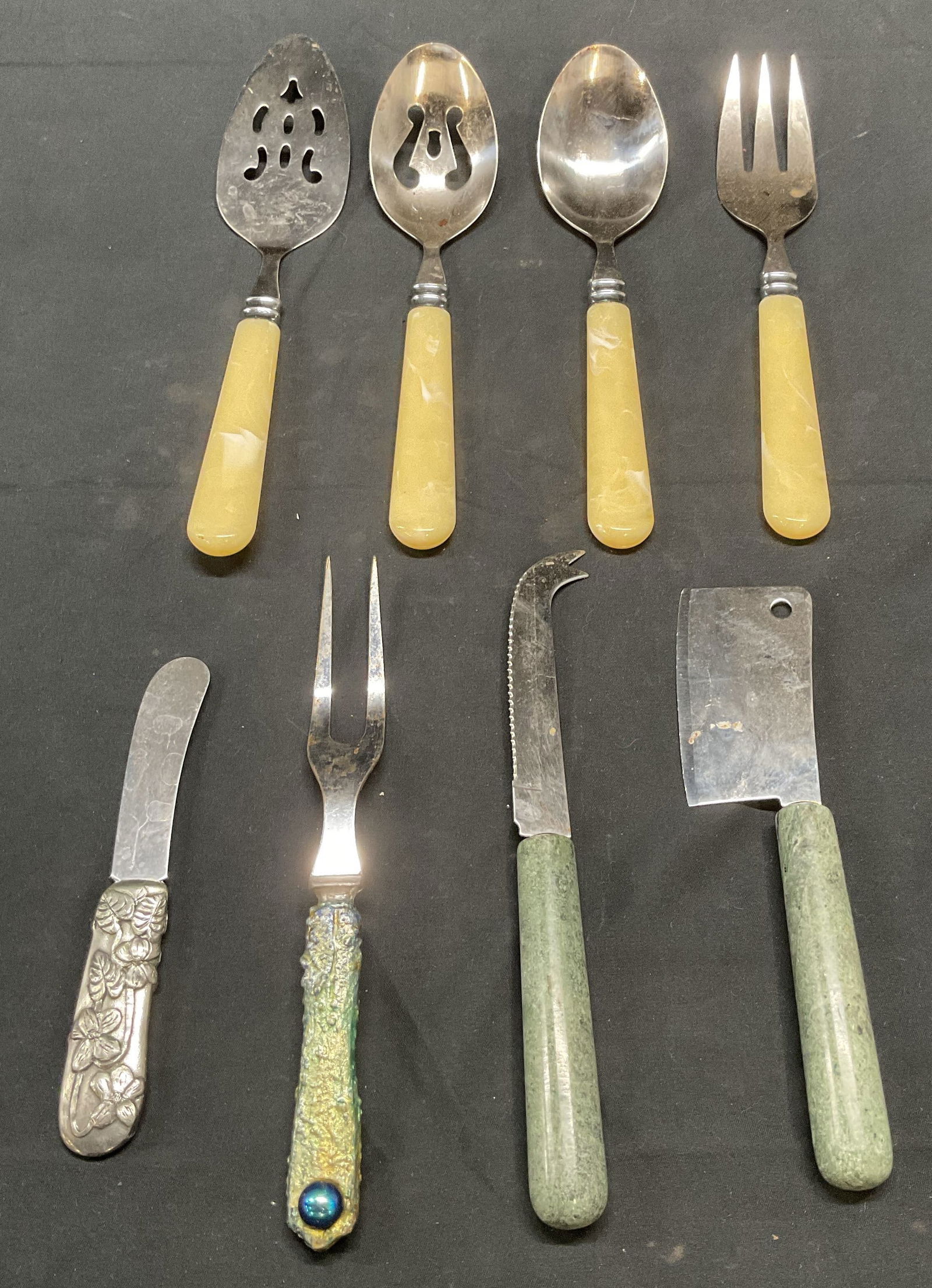 Lot 8 Vintage Lucite & Stone Handle Flatware: Lot of 8 vintage flatware pieces. 4 cream toned lucite handle pieces. 2 spoons, 1 server, and 1 fork. 1 silver tone handle knife with floral motif. 1 iridescent green handle fork. 2 green stone handle