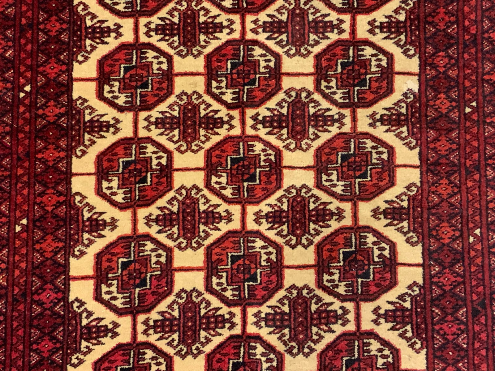 Vintage Persian Bokhara Medallion Pattern Rug: A vintage Persian Bokhara rug featuring a medallion pattern to the center. Primarily red, black, and cream hues. Fringe trim. No material tag present, possibly crafted from wool. Measures approx. 46W 