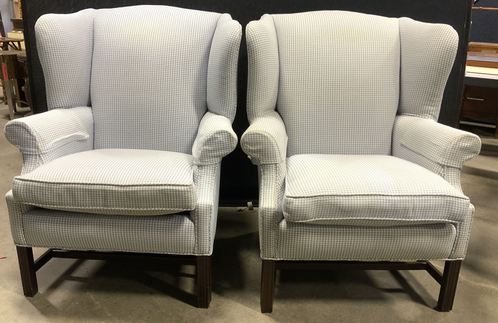 Pr Houndstooth Upholstered Wingback Chairs: Lot includes 2 chairs. Chairs appear to be vintage. Each chair has winged backrest. Chairs each have light blue and white toned houndstooth upholstery. Each chair has brown toned wooden legs with stre