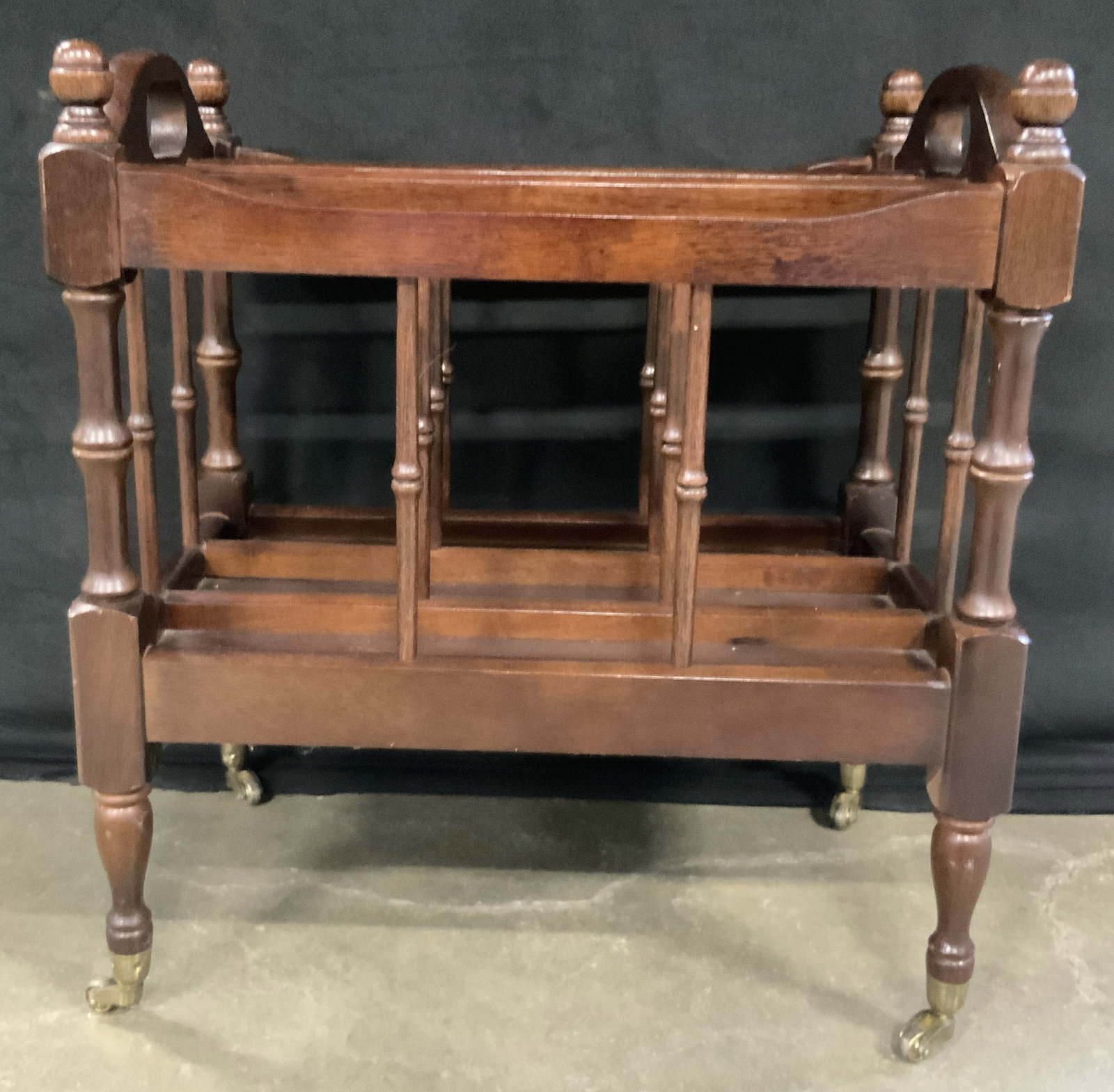 Vintage Wooden Magazine Rack on Casters: A vintage wooden magazine rack / document organizer. Rich brown hued finish. Four brass toned metal casters to the legs. Canterbury style. Measures approx. 20.5H x 19W x 12D in. Some surface wear cons
