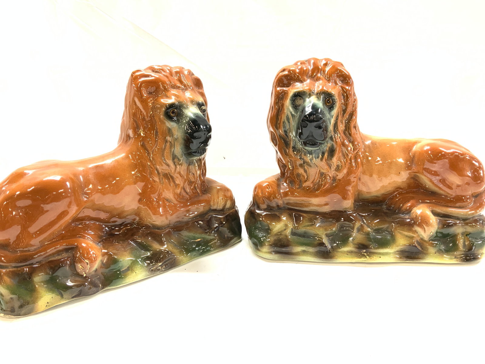 Pair Antq Staffordshire Porcelain Mantle Lions: PAIR OF VICTORIAN STAFFORDSHIRE POTTERY LIONS, made in England. Possibly dated in the last quarter of the 19th century. The recumbent lions are hand painted and set with glass eyes. One eye missing fr