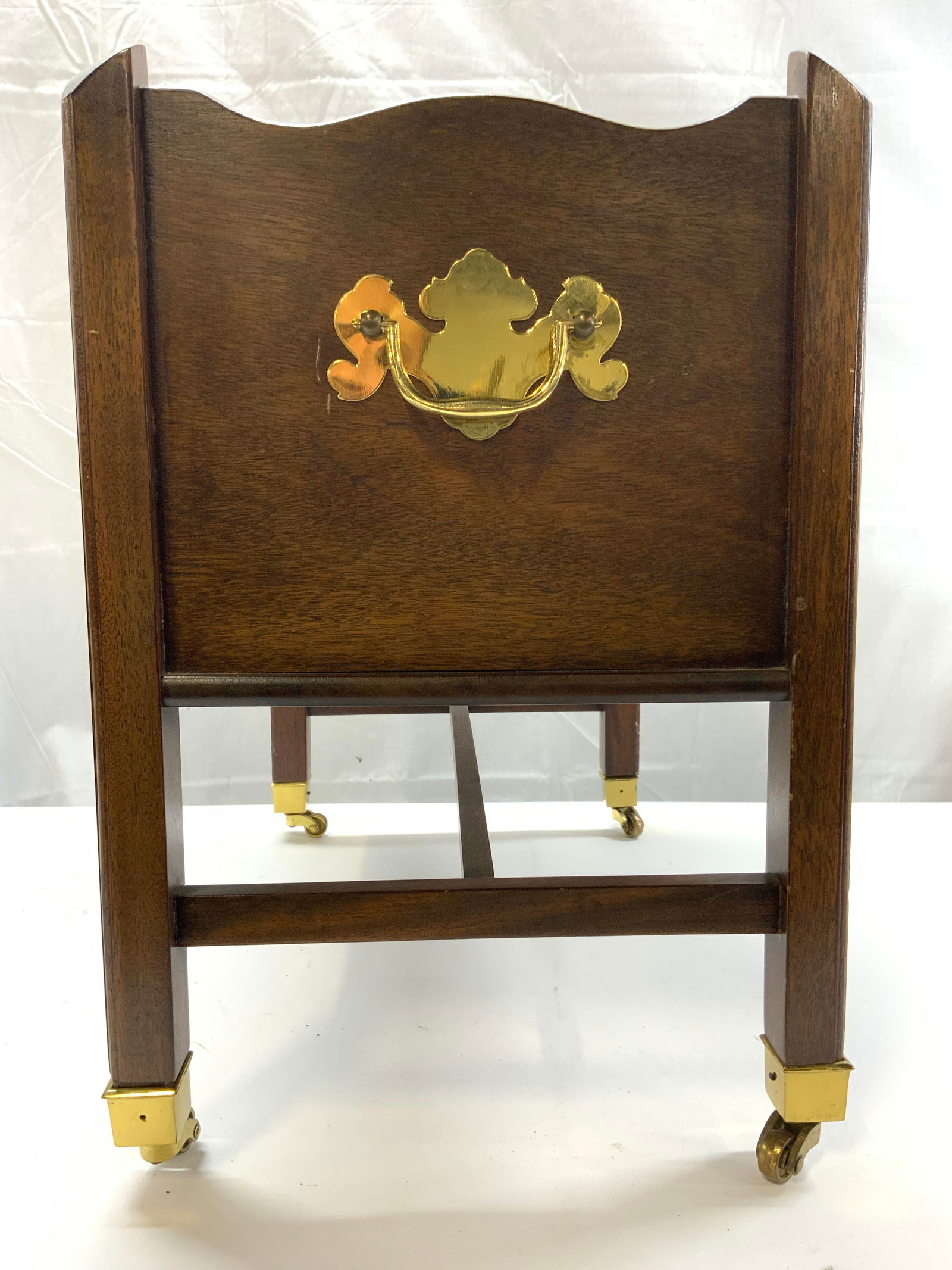 Wooden Canterbury W Handles On Casters: Canterbury is brown toned, appears to be wooden, possibly veneer. Piece sits on 4 gold toned brass wheels. Canterbury has gilt metal handle on each side. Piece measures approximately 17 inches tall 18