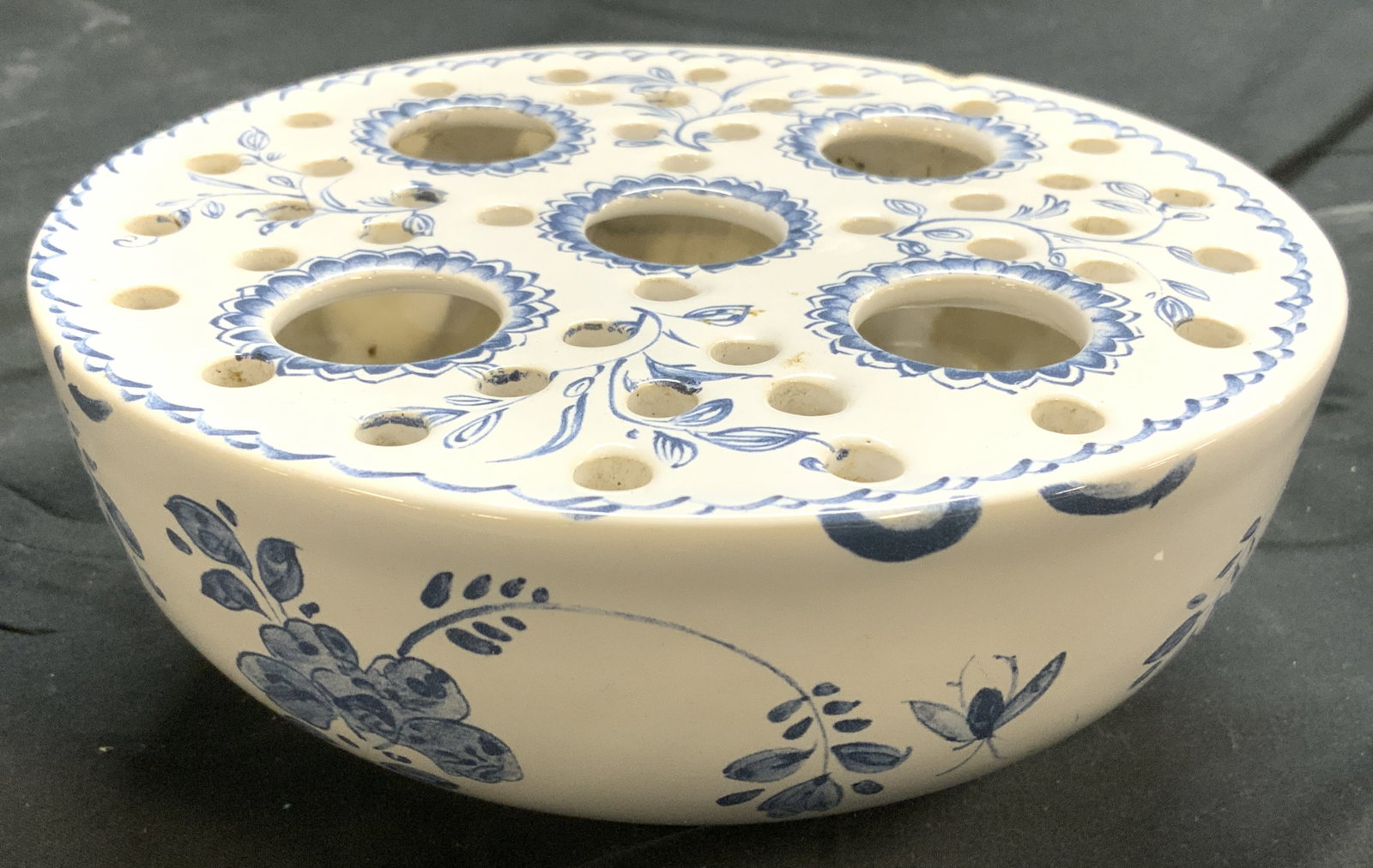 MOTTAHEDEH Vntg Delft Style Porc Flower Frog: Underside reads MOTTAHEDEH PORTUGAL. Piece is white toned and porcelain with blue toned floral, leaf, & vine detail. Flower frog has bowl form. Piece measures approximately 6.75 inches diameter 3 inch