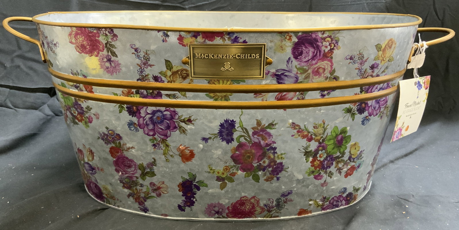 MACKENZIE CHILDS Flower Market Beverage Bucket: Tag reads MACKENZIE CHILDS FLOWER MARKET BEVERAGE BUCKET. Piece is silver toned and metal with intricate multi toned floral and leaf detail. Piece has gilt metal accents and handles. Vessel has oval f