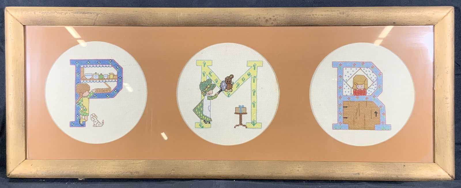 Framed Alphabet Lettered Needlepoint Motifs: Needlepoint embroidery. Three motifs of needlepoint lettering. Letter P has a girl and a puppy reaching for a cookie tin on a shelf. Letter M has a maid dusting off a teddy bear. Letter R has a girl l