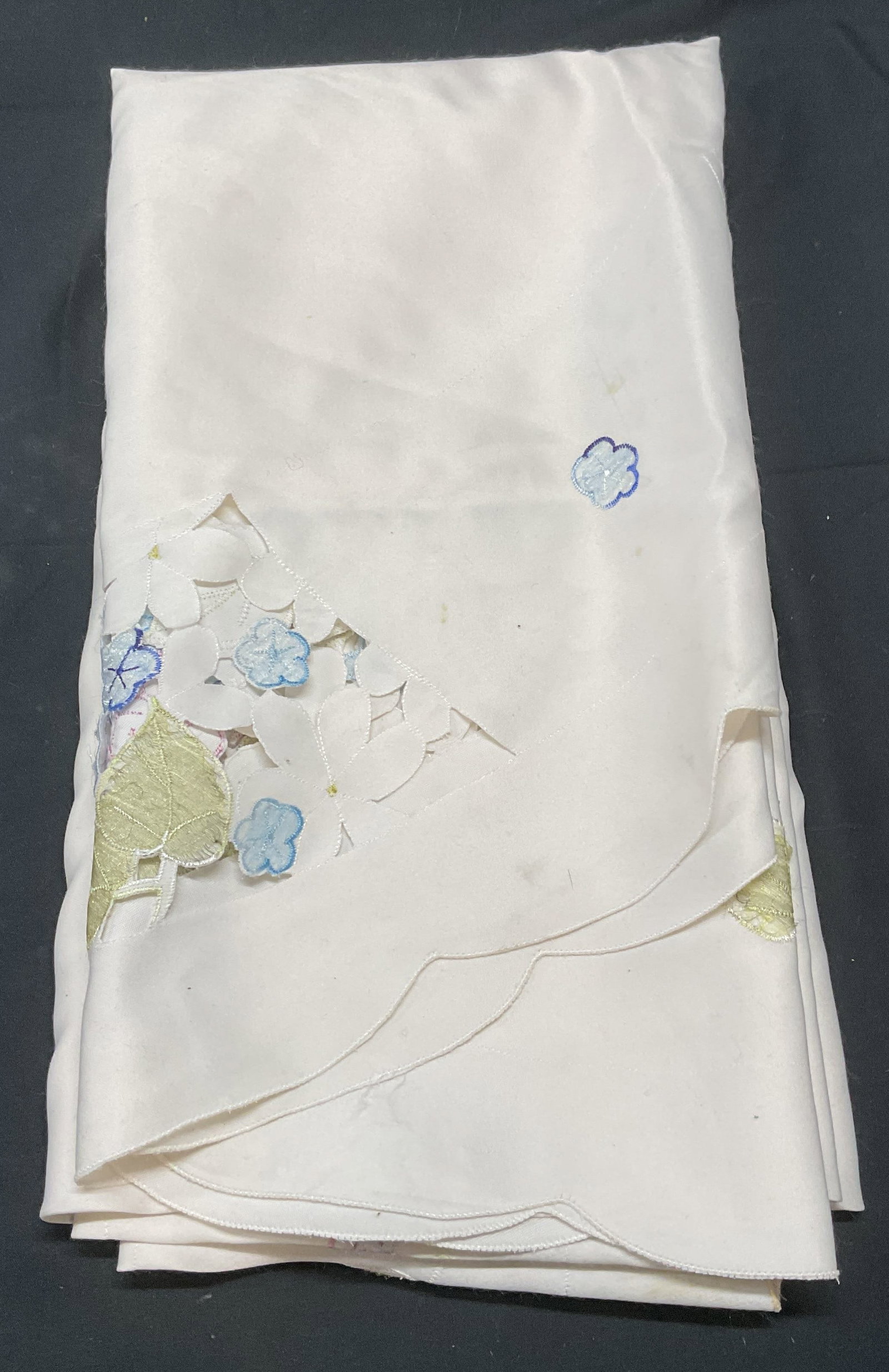 White Embroidered Floral Oval Tablecloth: White oval tablecloth with cutout detail and embroidered floral motif. Measures approx. 66 inches wide. Material feels synthetic. Some wear to material including blemishes observed. Tablecloth, white 