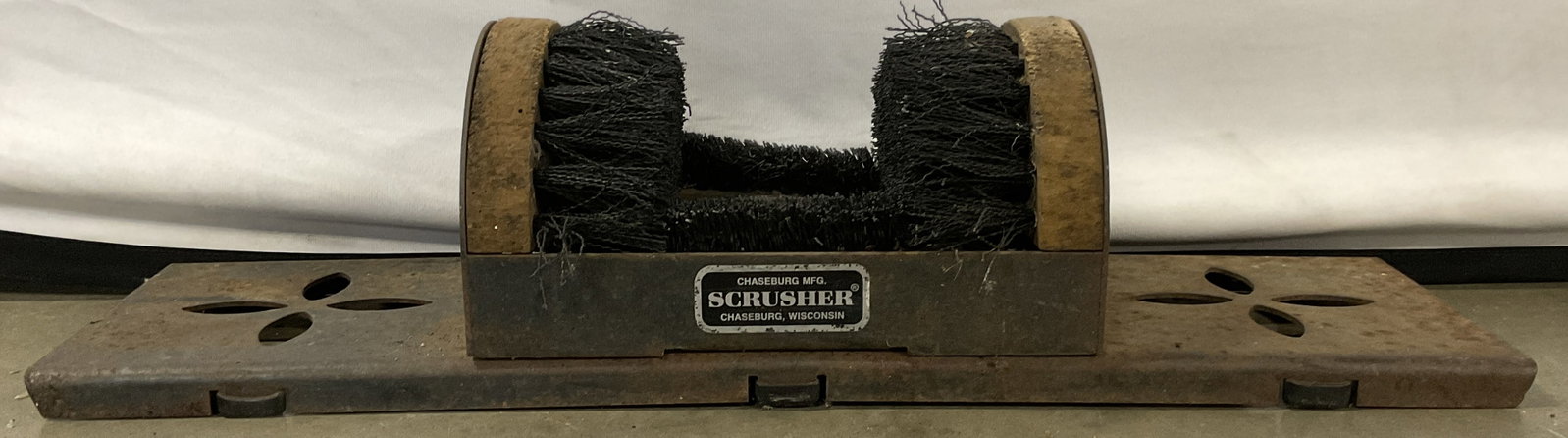 CHASEBURG MFG. SCRUSHER Iron Boot & Shoe Cleaner: A boot and shoe cleaner fitted with a wooden bristled brush affixed to pierced metal, appears to be iron. Plaque to obverse reads CHASEBURG MFG. SCRUSHER CHASEBURG, WISCONSIN. Measures approx. 5H x 22