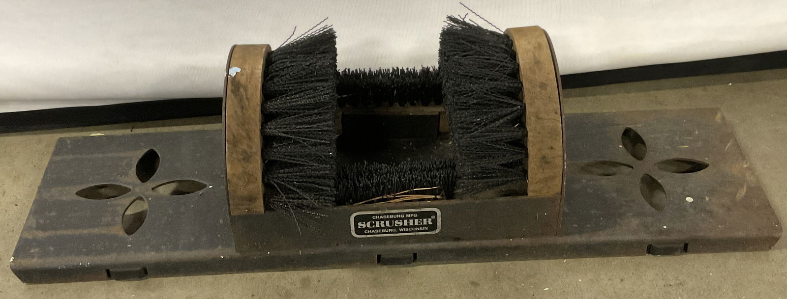 CHASEBURG MFG. SCRUSHER Iron Boot & Shoe Cleaner: A boot and shoe cleaner fitted with a wooden bristled brush affixed to pierced metal, appears to be iron. Plaque to obverse reads CHASEBURG MFG. SCRUSHER CHASEBURG, WISCONSIN. Measures approx. 5H x 22