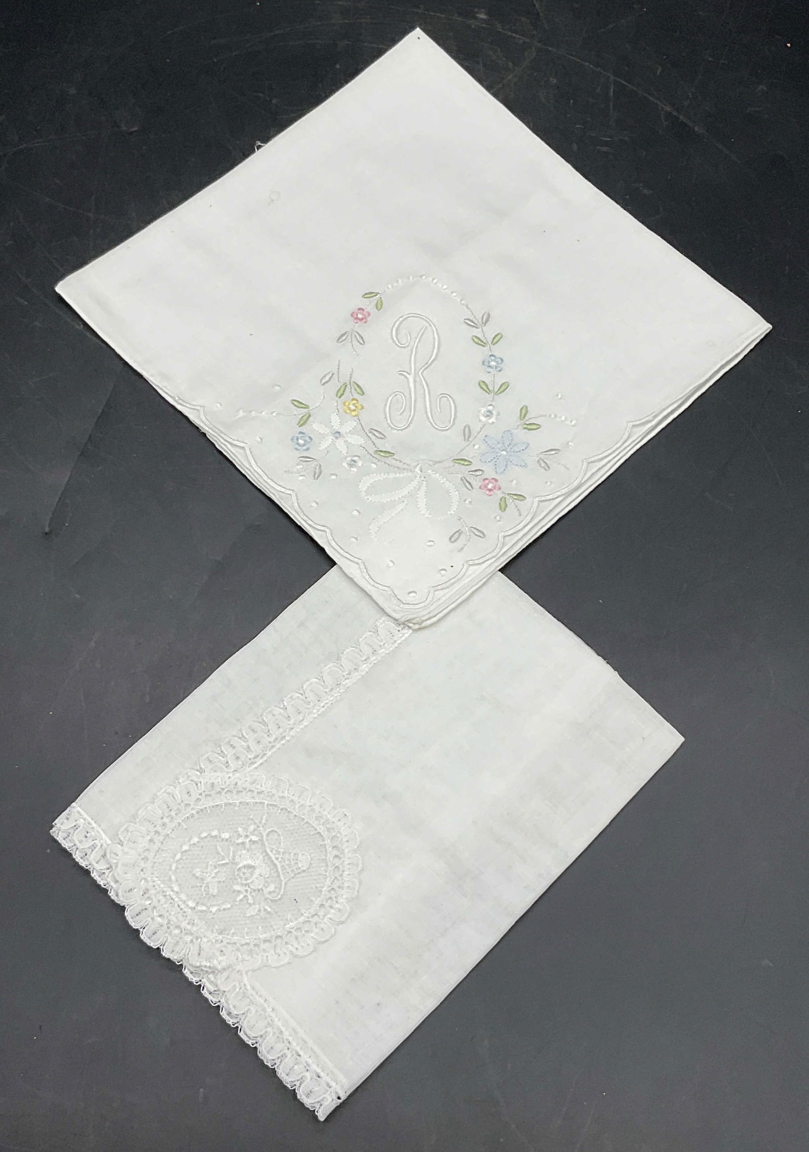 Lot 2 Vintage White Embroidered Handkerchiefs: Two vintage white embroidered handkerchiefs. Both pieces feature floral motifs. One piece features the letter R embroidered to one side and accented by a scalloped edge. Soft muted pink, green, yellow