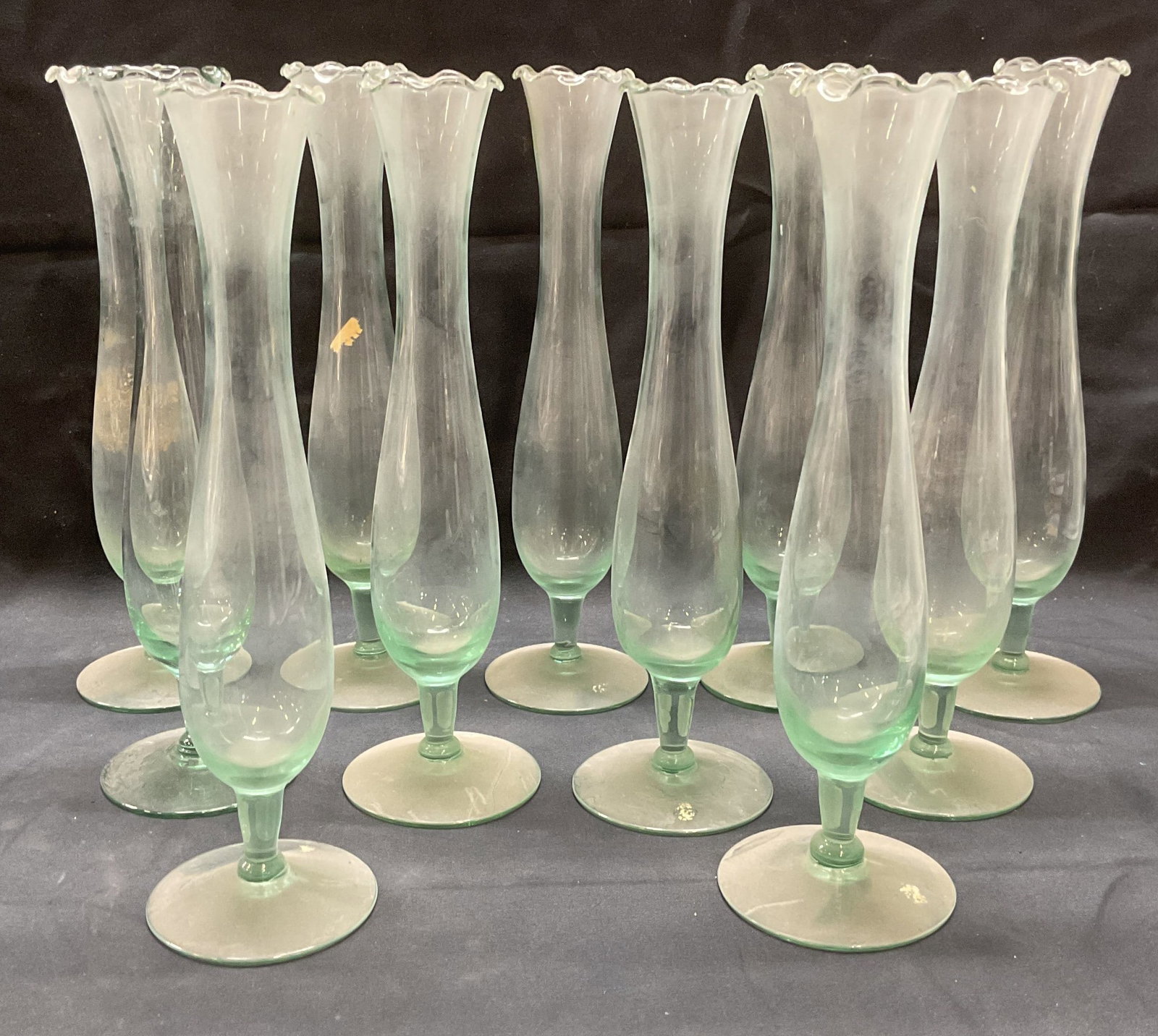 Set 11 Transparent Green Glass Footed Vases: Set of 11 transparent green toned glass vases. Footed with handkerchief rims. Measure approx. 2.75 x 10.5 inches each. All pieces have some surface wear including scratching and residue observed. Vase