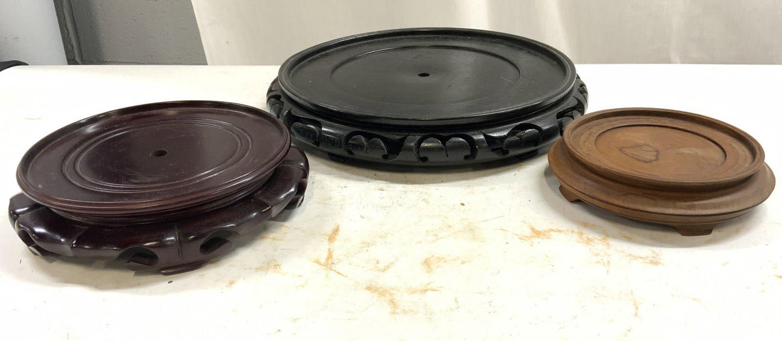 3 Asian Carved Wood Pedestals Stands 1ft Dia &More: Lot includes 3 Asian stands. Each piece is wooden. Lot includes 1 black, 1 light brown and 1 mahogany toned stand. Largest stand has pierced detail at sides. Each stand is footed. Largest stand measur