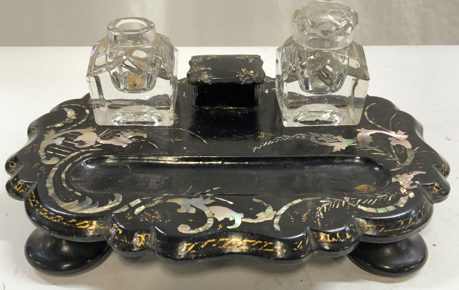 Vntg Lacquer, Mother Of Pearl, & Glass Inkwell: Inkwell is black toned & lacquered. Piece has mother of pearl scroll, leaf & vine detail. Inkwell has 4 feet. Piece has 2 glass basins. One includes lid. Inkwell measures approx 10.5 inches long 8 inc