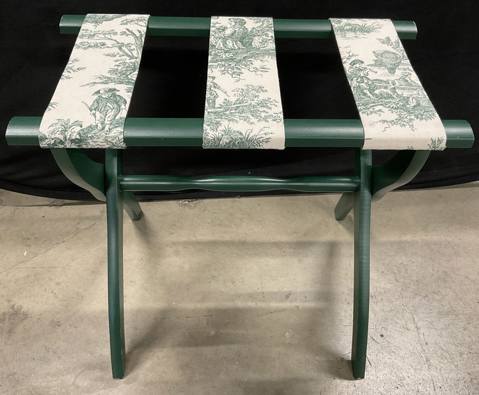 Scheibe Green Toile Fabric Luggage Rack: A collapsible toile style fabric luggage rack / suitcase rack. Primarily green hues. Open the piece measures approx. 23W x 13D x 19.75H in. Tag to underside reads Scheibe. Losses to paint present. Som