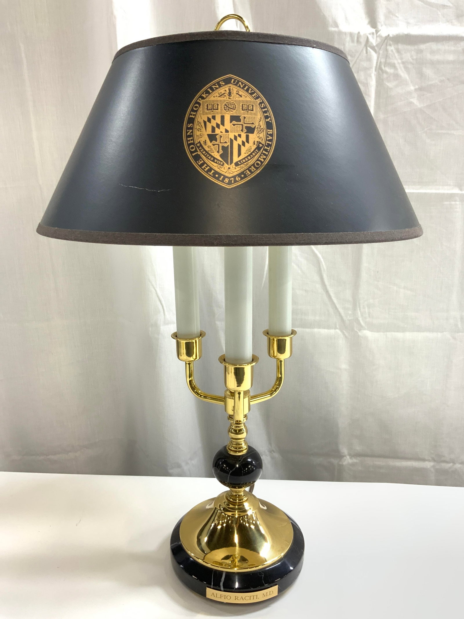 JOHN HOPKINS UNI Shade Monogrammed Candelabra Lamp: Shade reads THE JOHN HOPKINS UNIVERSITY BALTIMORE. Base of lamp monogrammed ALFIO RACITI, MD. Lamp has 3 arm candelabra form. Piece has gilt metal and black toned marble areas. Lamp includes finial. P