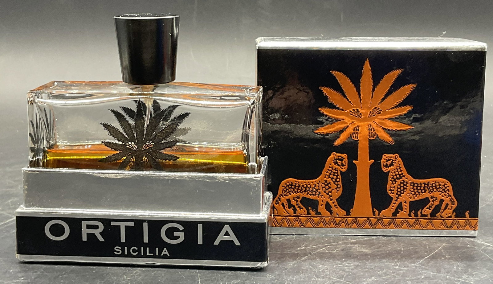 ORTIGIA SICILIAN Fragrance Bottle W/ Original Box: ORTIGIA SICILIAN AMBRA NERA Fragrance Bottle With the Original Box. The box measures approx. 4.25H x 4W in. Some liquid to the fragrance bottle. Pieces have wear consistent with age, use, and exposure